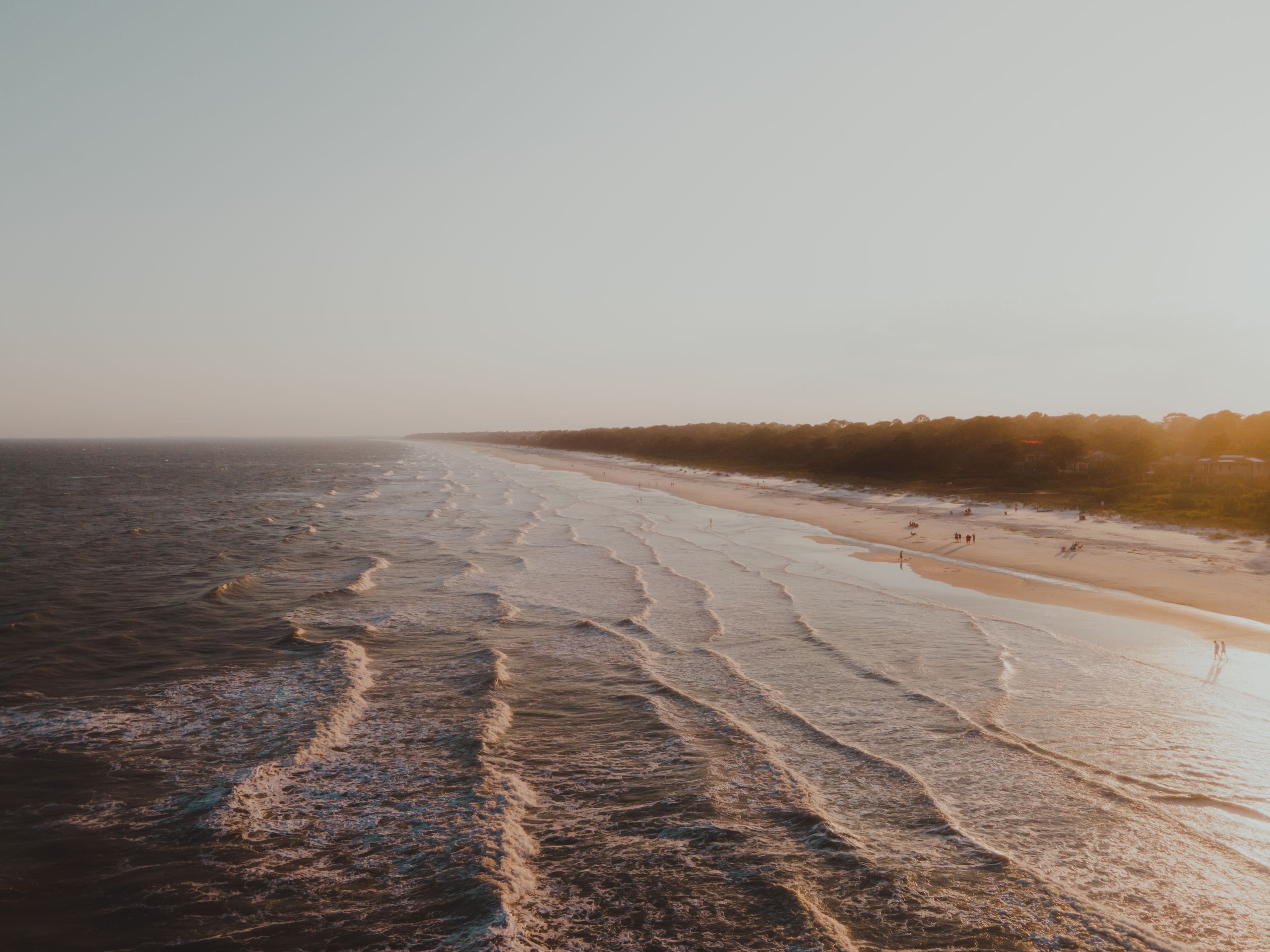 Picturesque aerial view of ocean waves gently crashing on a sandy shoreline at sunset, creating serene coastal scenery.